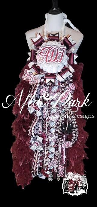 Maroon and silver luxury homecoming mum with white flower center reading ADT, feather boa trim, senior year and cheerleading embellishments by After Dark Custom Designs